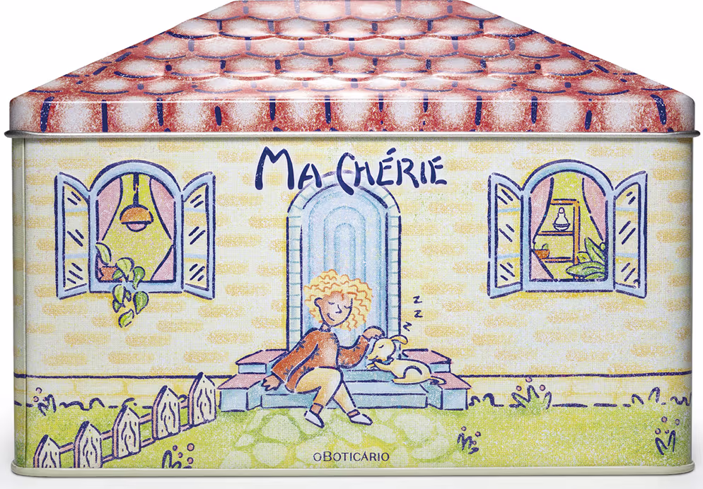 Caixa retangular de metal decorada com ilustrações coloridas. A tampa apresenta um padrão de telhas vermelhas e brancas. Na parte frontal, há uma cena ilustrada com uma figura feminina loira sentada em um banco, segurando um livro, em frente a uma casa.