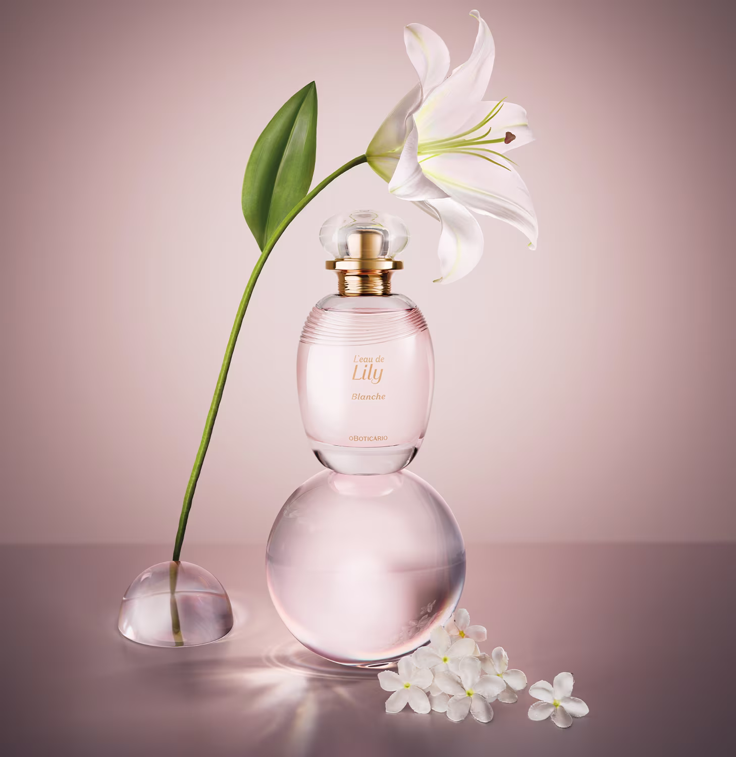O rótulo do frasco exibe o nome "Leau de Lily Blanche" em letras douradas. Ao lado do frasco, há uma flor de lírio branca e uma folha verde. O fundo da imagem é em tons de rosa, complementando a aparência delicada e refinada.