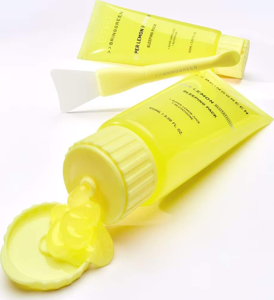 Tubo de creme amarelo da marca Bringgreen, com rótulo destacando o nome do produto "Lemon Sleeping Pack". Embalagem cilíndrica com tampa e aplicador, apresentando também uma espátula branca ao lado.