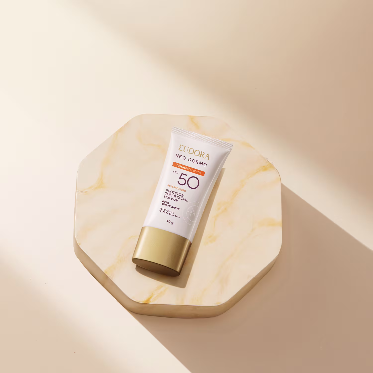 O produto apresentado na imagem é um protetor solar da linha Neo Dermo da marca Eudora. Trata-se de um tubo de cor branca e dourada, com o rótulo indicando um fator de proteção solar 50. O produto é descrito como um "Defensor Solar" que protege a pele.