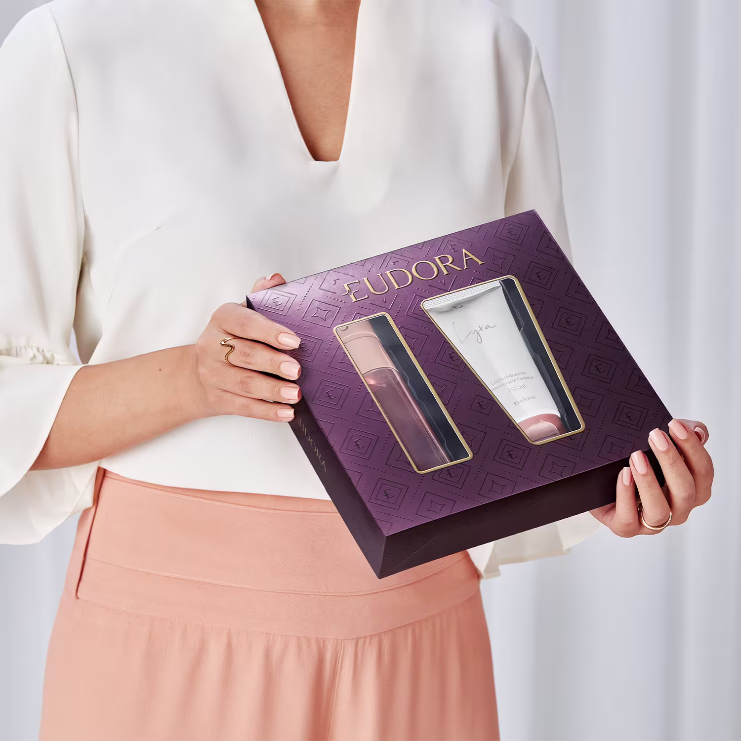 A imagem mostra uma mulher segurando a caixa de presente Eudora Lyra, em tom roxo e detalhes em dourado.