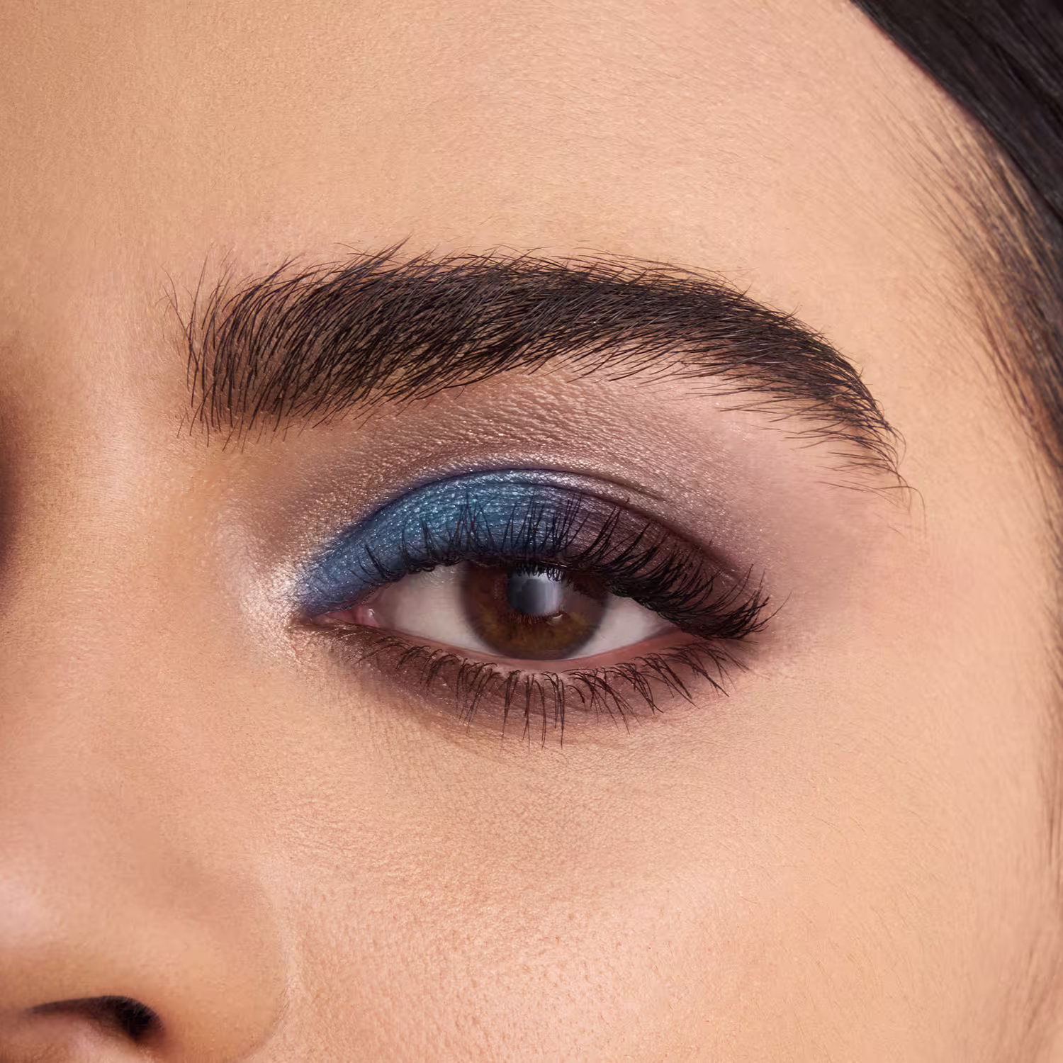 A imagem mostra um olho com maquiagem aplicada. Pode-se ver uma sombra azul escura aplicada na pálpebra, realçando os cílios escuros e bem definidos. As sobrancelhas estão preenchidas e bem delineadas.