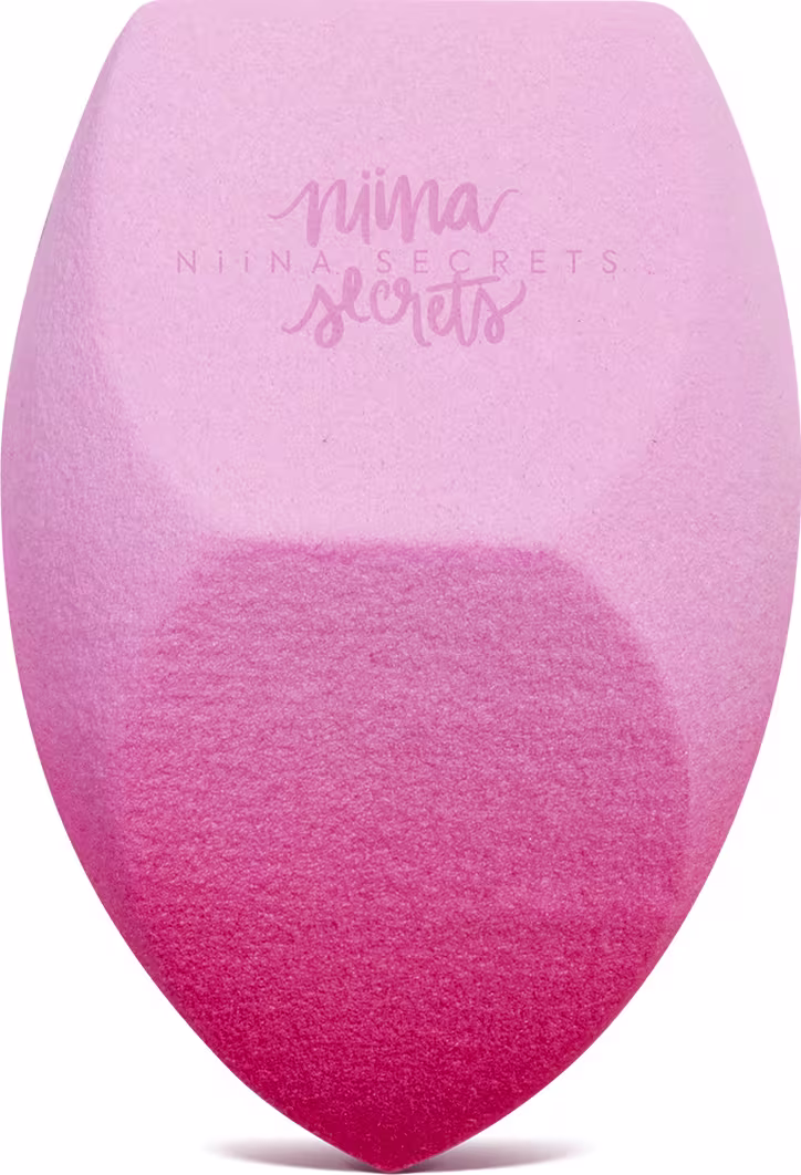 O produto apresentado é uma esponja para maquiagem da marca Niina Secrets, com uma coloração degradê de rosa claro a rosa escuro. Possui um formato arredondado e achatado em diferentes partes.