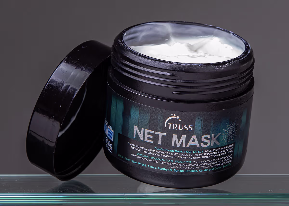 A imagem mostra um pote de uma máscara capilar chamada "Net Mask" da marca Truss. O pote é preto com detalhes azuis e contém uma máscara branca cremosa dentro.