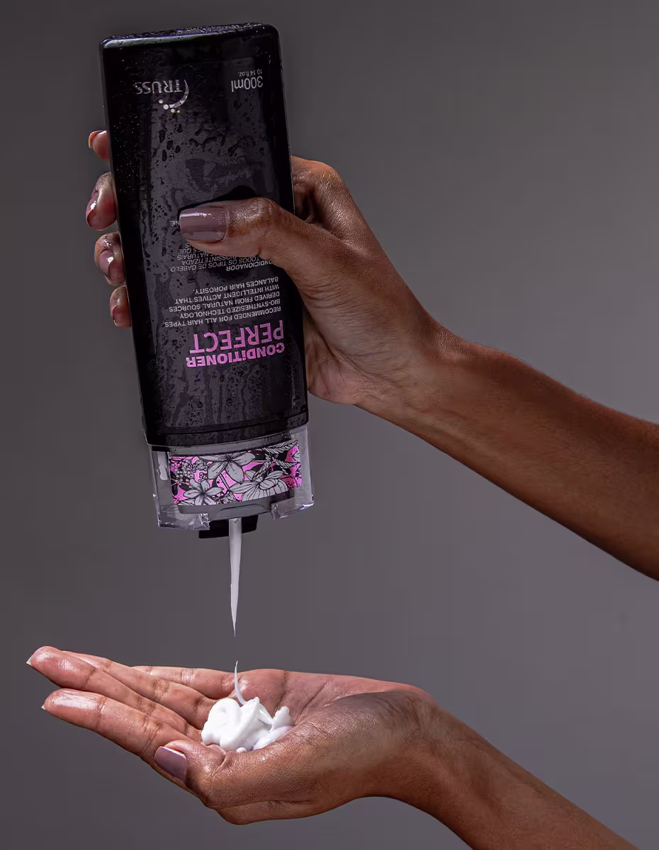 A imagem mostra o Condicionador TRUSS Perfect. O líquido está sendo despejado do frasco em uma mão feminina, mostrando a espessura do produto.