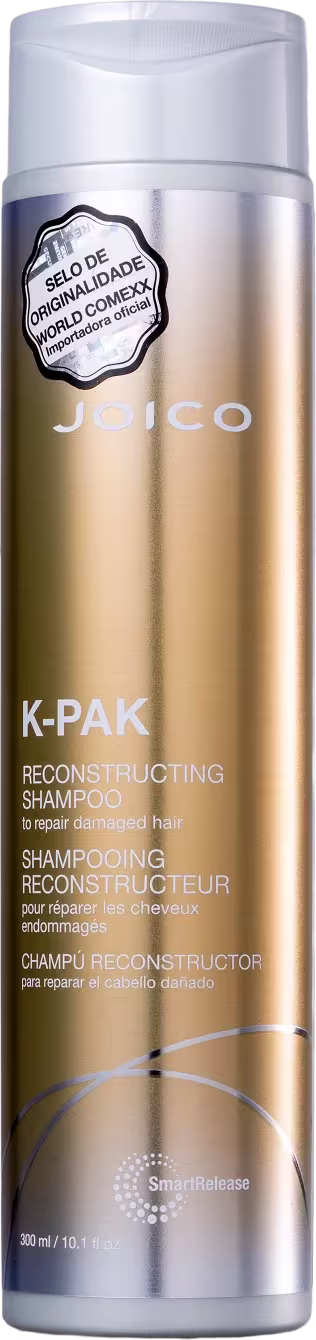 Produto de reconstrução capilar Joico K-PAK. Frasco cilíndrico de plástico transparente com tampa branca. Embalagem dourada metálica com detalhes em branco. Rótulo com o nome do produto "K-PAK Reconstructing Shampoo" em várias línguas.