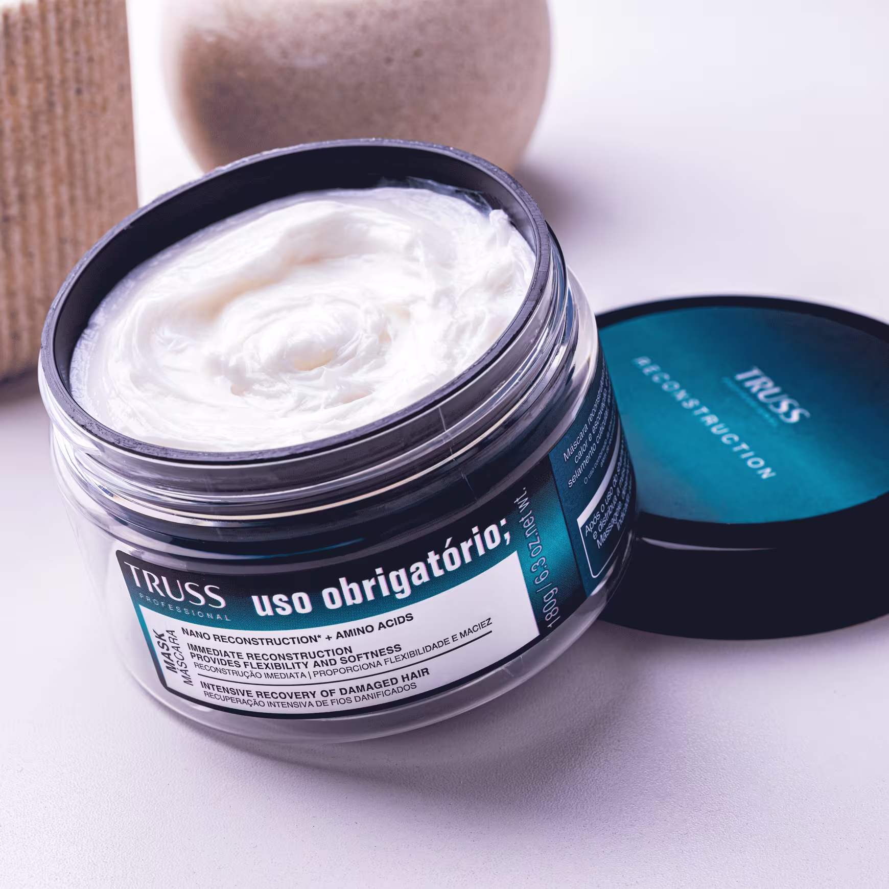 Produto de tratamento capilar da linha TRUSS Uso Obrigatório. Embalagem em pote plástico preto brilhante com tampa azul claro. Rótulo com texto "TRUSS Reconstruction" e descrições.