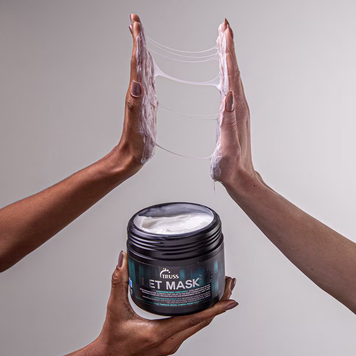Máscara capilar "Net Mask" da marca TRUSS. O produto tem uma cor branca cremosa visível. As mãos femininas segurando o pote têm um tom de pele moreno avermelhado.