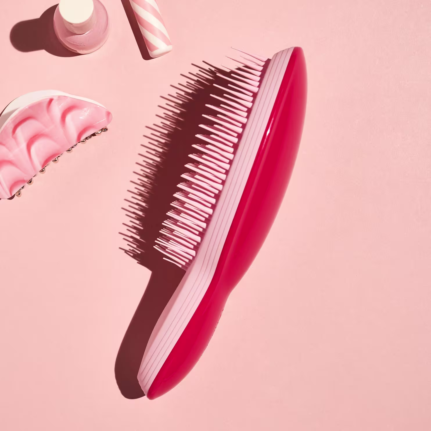 A escova possui um cabo longo e fino de cor rosa vibrante. A parte da escova com cerdas é rosa escuro e tem uma forma arredondada. Não há texto ou rótulos visíveis na escova.