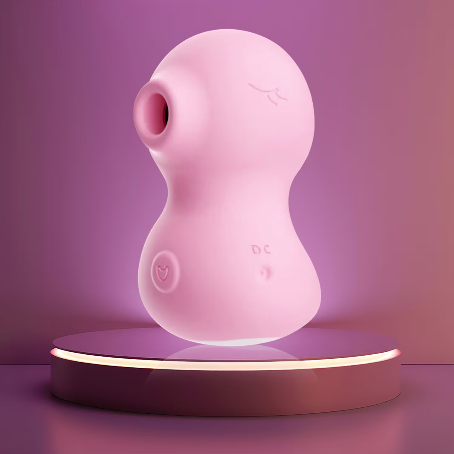 O produto apresentado é um objeto de design em formato oval, com uma superfície lisa e brilhante em tom de rosa claro. Há um pequeno texto impresso na superfície, indicando "DC". O objeto está posicionado sobre uma plataforma iluminada, em um ambiente com fundo degradê em tons de rosa e roxo.