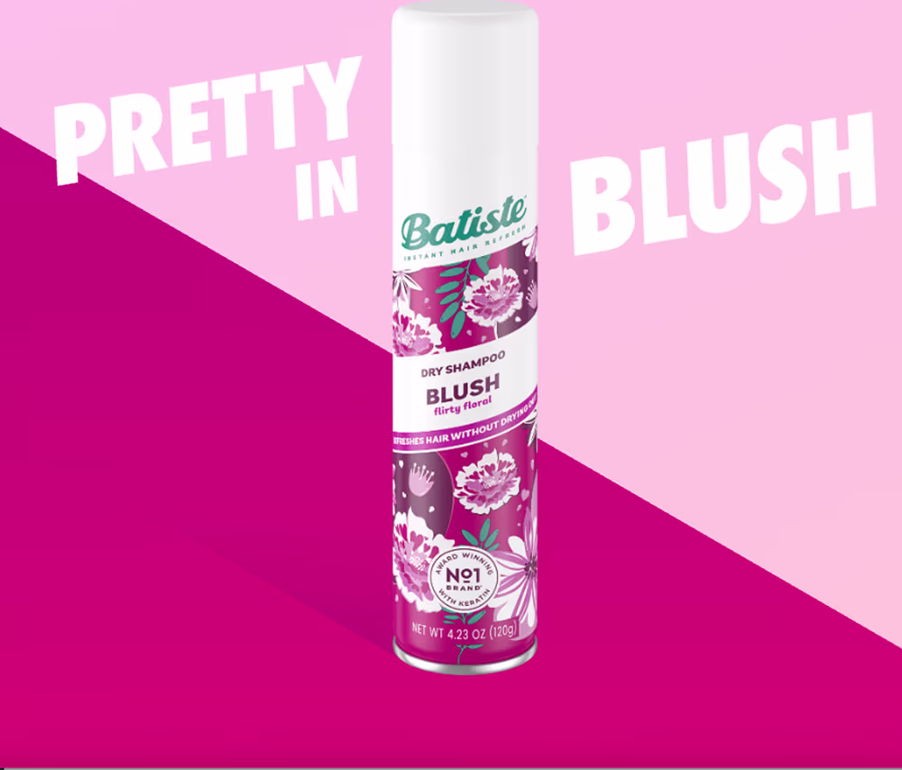 Shampoo a seco da marca Batiste, na fragrância "Blush". . O rótulo destaca o nome da marca e o tipo de produto, "Dry Shampoo Blush". O frasco possui um tamanho (120g). A imagem é apresentada em um fundo rosa vibrante, criando um contraste com a embalagem.