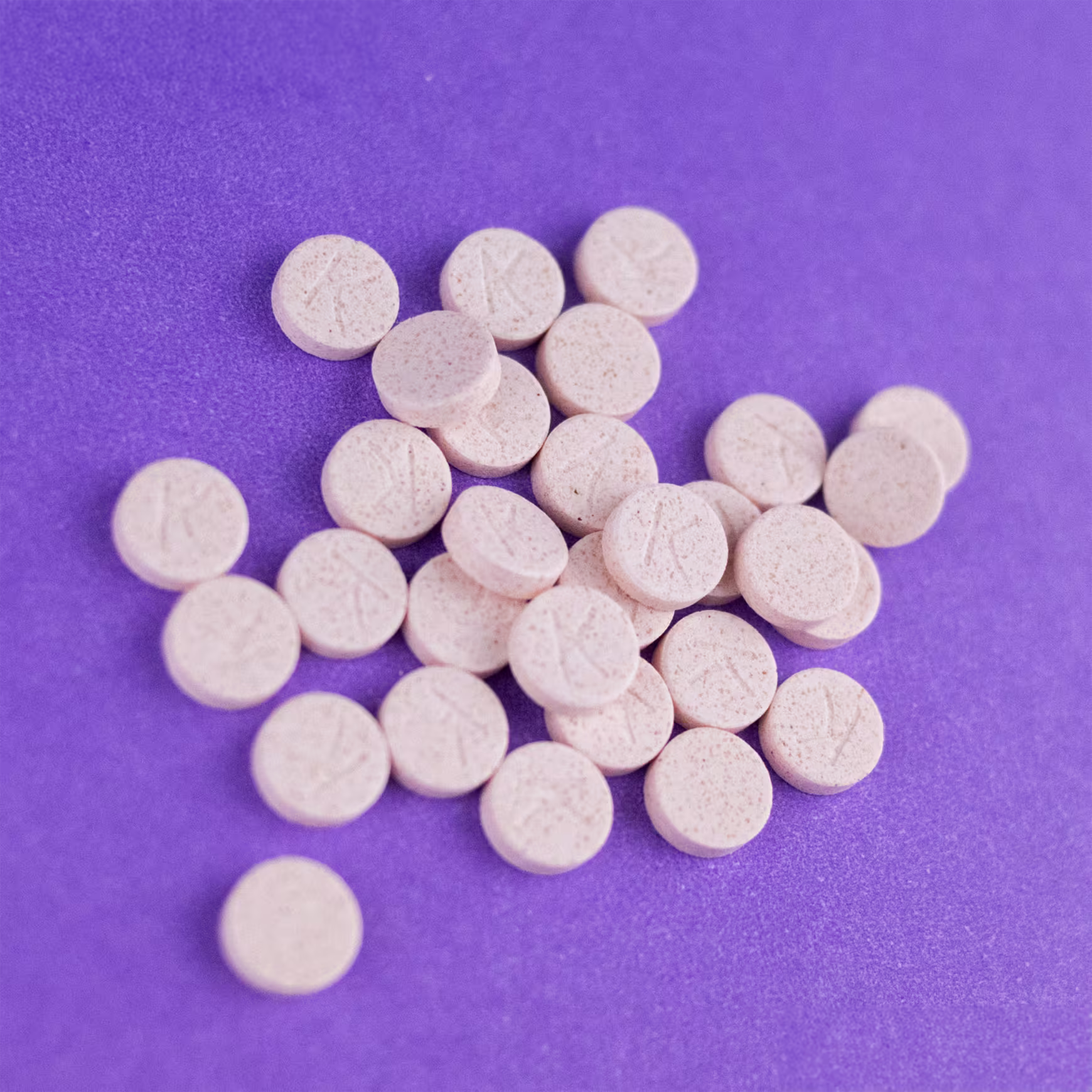 A imagem mostra os comprimidos brancos em uma superfície roxa.
