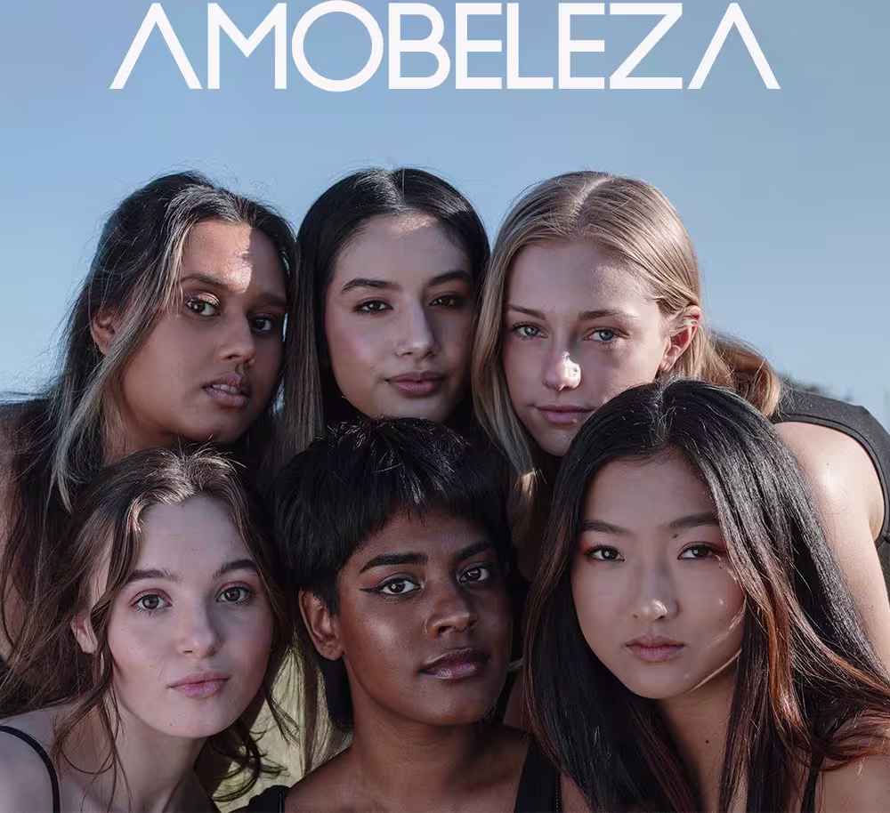 A imagem mostra um grupo de cinco modelos mulheres de diferentes etnias e tons de pele, posando juntas. Elas têm expressões faciais sérias e maquiagem natural. O texto "AMOBELEZA" aparece em letras maiúsculas brancas na parte superior.