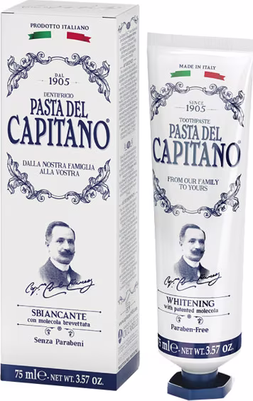 A imagem mostra a caixa retangular e o creme dental Sbiancante da marca italiana Pasta Del Capitano 1905. Os produtos têm um design vintage cor branca com detalhes ornamentados em azul e a imagem de um homem, provavelmente o fundador da marca, estampada.