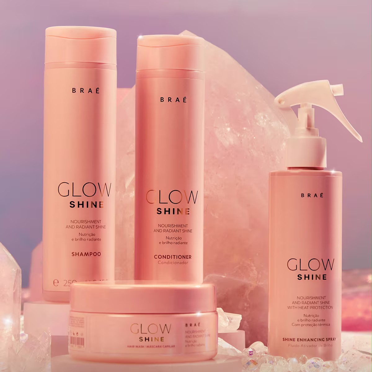 Produtos de cuidados capilares da linha Glow Shine da marca Braé. Shampoo e condicionador em frascos cilíndricos rosados. Creme de tratamento em pote rosado. Spray de brilho em frasco bomba rosado. Embalagens com o nome da linha "Glow Shine".