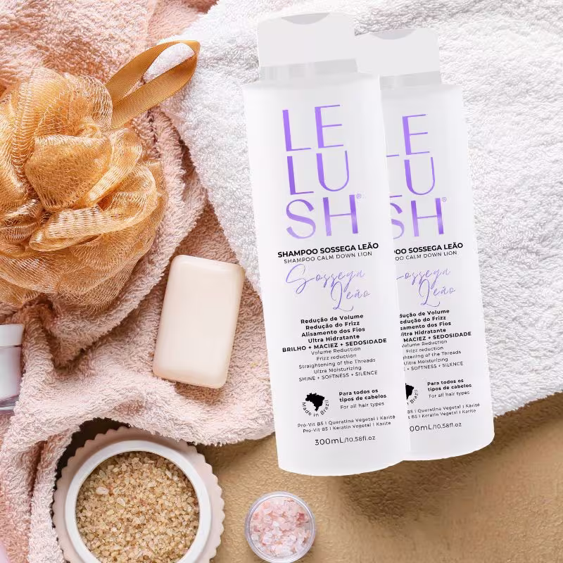 A composição da imagem transmite uma atmosfera aconchegante e relaxante, remetendo aos momentos de cuidados pessoais e autocuidado. Nela há duas embalagens de shampoo sobre uma toalha branca ao lado de itens de higiene pessoal, como sabonetes e sais.