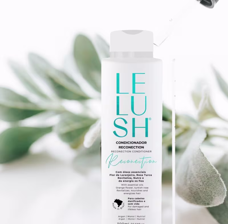 A imagem mostra o frasco do condicionador com embalagem branca e letras azuis. O produto está posicionado sobre um fundo claro, rodeado por folhas verdes, aparentemente de uma planta, criando um ambiente natural e orgânico.