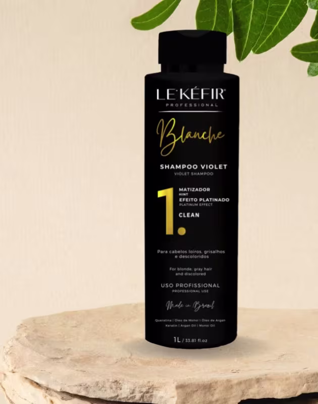 A imagem mostra o frasco do shampoo posicionado junto a longos cabelos loiros espalhados, pertencentes a uma pessoa que não é totalmente visível na foto.