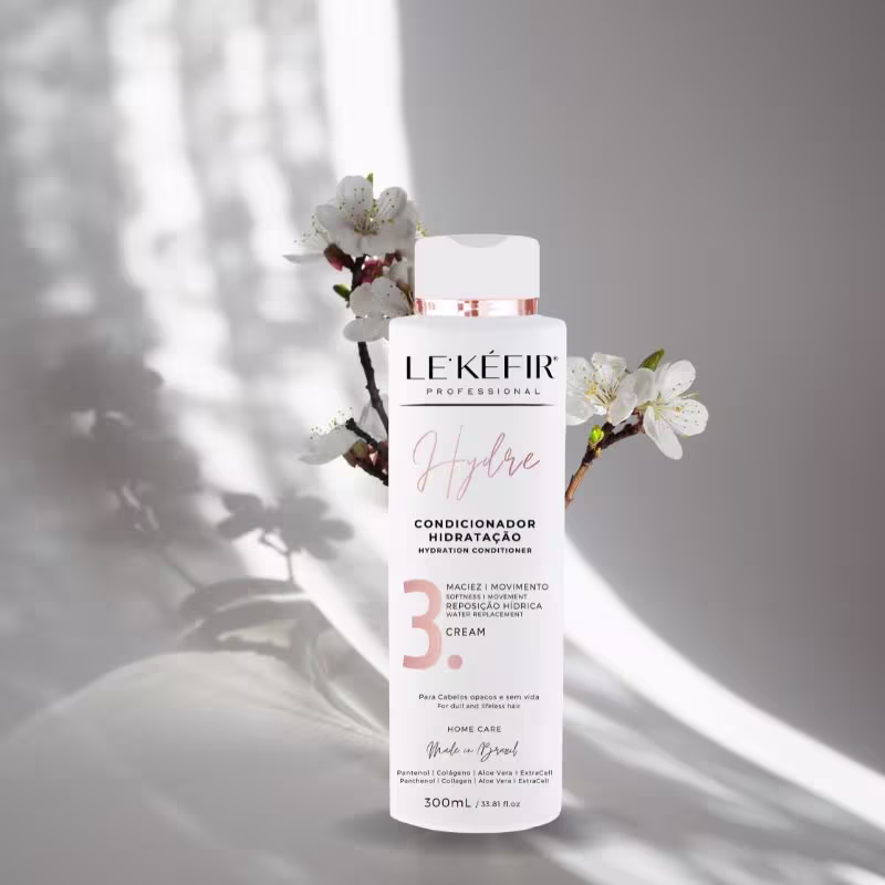 Em primeiro plano, há um frasco da marca Le'Kéfir, identificado com o condicionador. Ao fundo compondo o cenário, há um galho com algumas flores de cerejeira, trazendo delicadeza e suavidade a imagem.