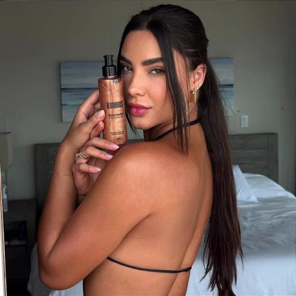 Mulher branca com a pele iluminada, segurando o frasco do gel iluminador Bloom