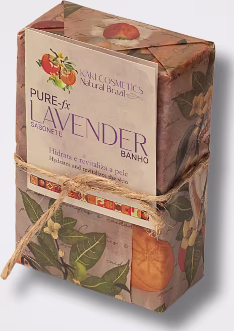 Caixa retangular de papelão com estampa de folhas e frutas alaranjadas. Rótulo com o texto "Pure & Lavender Banho". Fita de papel amarrada ao redor da caixa. Cores predominantes são marrom, laranja e verde. Embalagem com design rústico e natural.