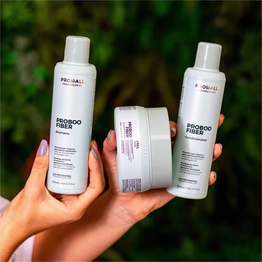 A imagem mostra uma mão feminina segurando 3 produtos da linha Proboo Fiber da marca Prohall Cosmetic.