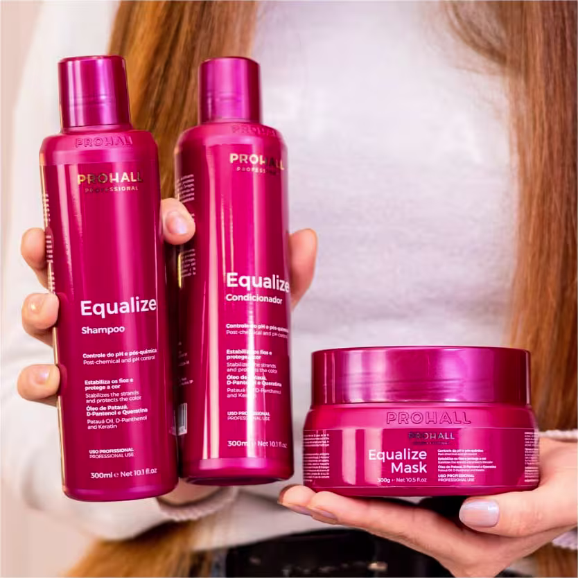 A imagem mostra um close up de uma mulher segurando produtos da linha Equalize, sendo um shampoo, um condicionador e uma máscara.