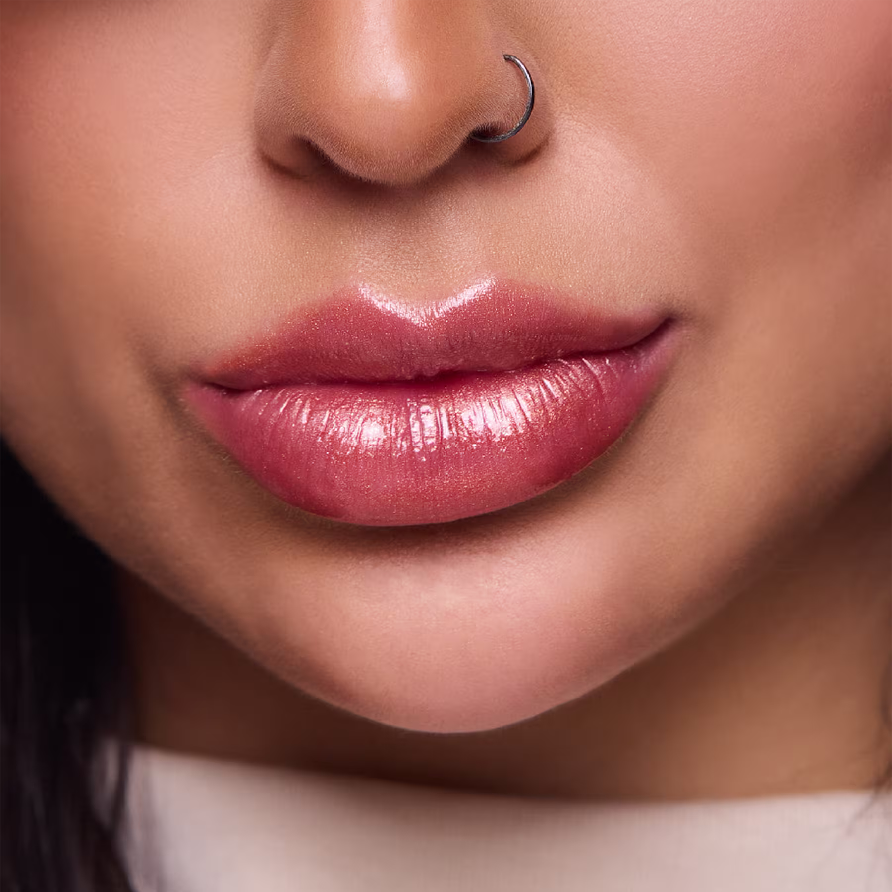 A imagem mostra um close-up dos lábios de uma mulher usando um brilho labial intenso marrom suave. Os lábios estão selados em um leve sorriso. O batom deixa os lábios com uma aparência sedosa e hidratada.