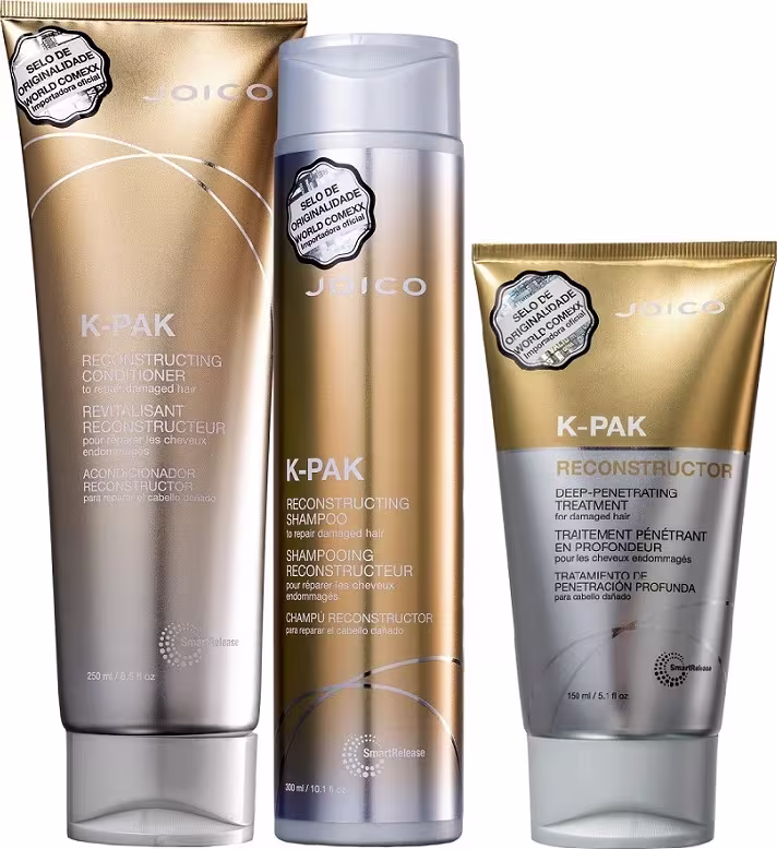 A imagem mostra três produtos da marca Joico, da linha K-Pak. São um condicionador reconstrutor, um shampoo reconstrutor e um tratamento profundo penetrante, todos em embalagens com cores douradas e prata.
