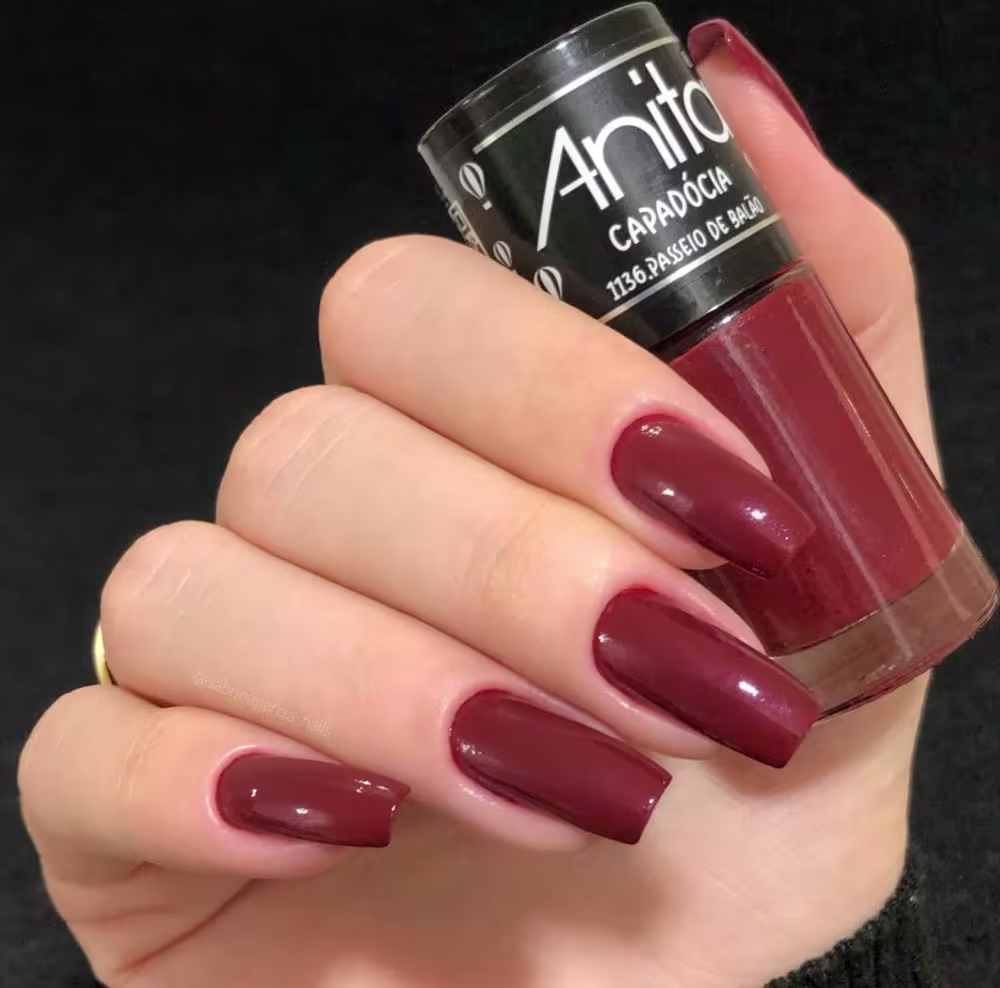 Modelo segurando o frasco de esmalte com suas unhas pintadas da mesma cor.