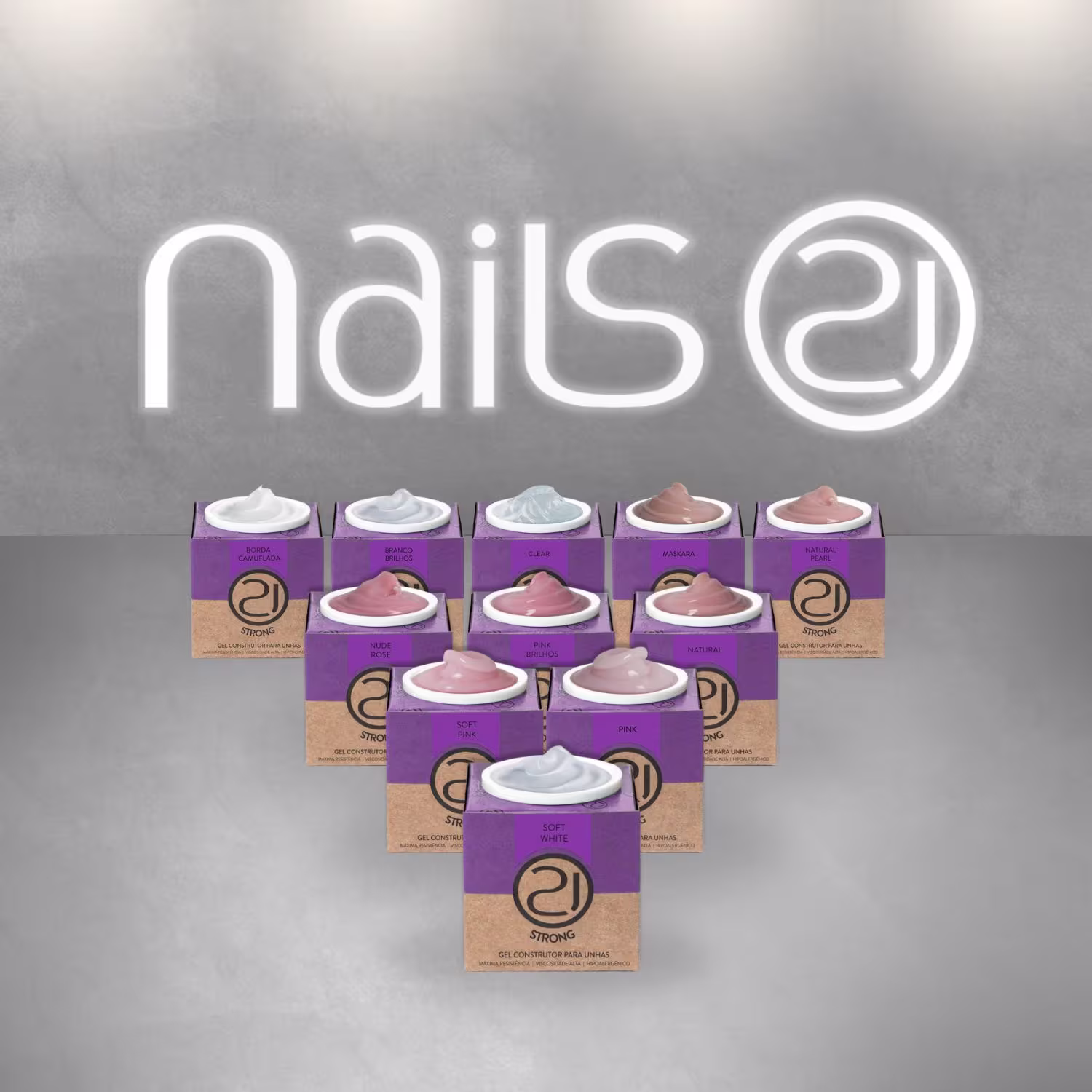 A imagem mostra uma variedade de géis reconstrutores para unhas da marca Nails 21. Há 11 pequenas embalagens retangulares com amostras do gel nas cores branca, nude e rosa claro. No topo, o nome "Nails 21" aparece em letras brancas contra um fundo cinza.