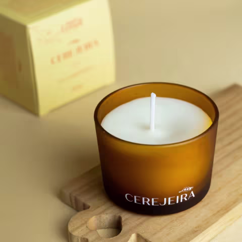 Vela aromática em embalagem de vidro âmbar da marca Cerejeira, com rótulo em destaque, posicionada sobre superfície de madeira.