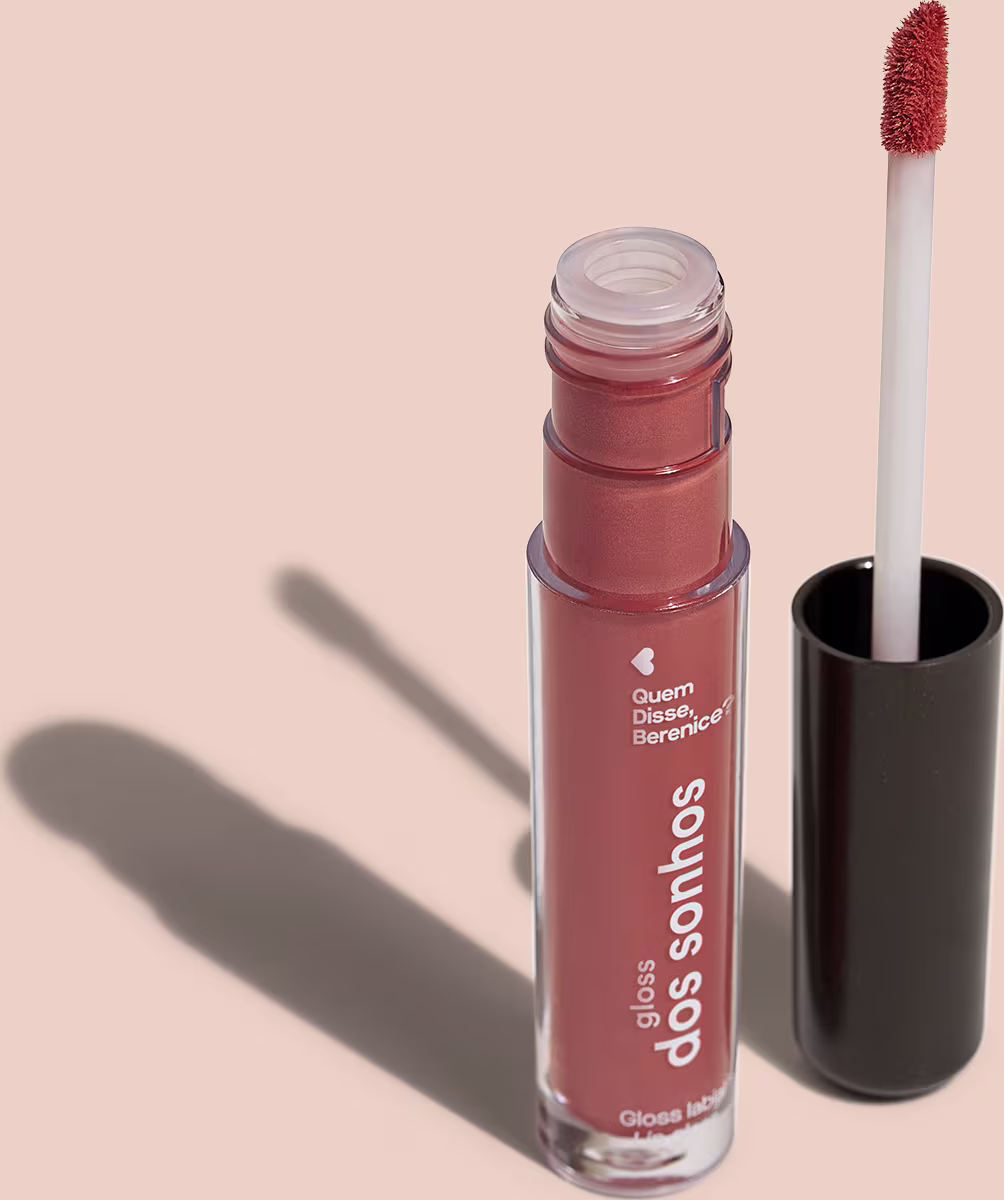 Frasco cilíndrico transparente contendo um gloss labial marrom. Rótulo na embalagem com o nome do produto "Gloss dos Sonhos" e a descrição "Quem disse, berence?". Ao lado, a tampa preta do produto, que acompanha um aplicador de espuma.