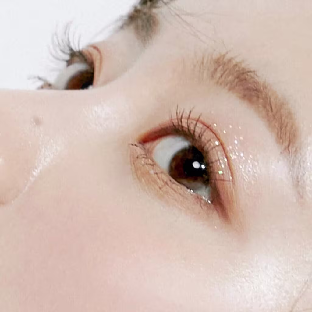 A imagem mostra um close-up de um olho humano com cílios longos e escuros, sugerindo um produto de beleza da marca rom&nd, possivelmente um rímel ou delineador, em um ambiente iluminado e com fundo claro.