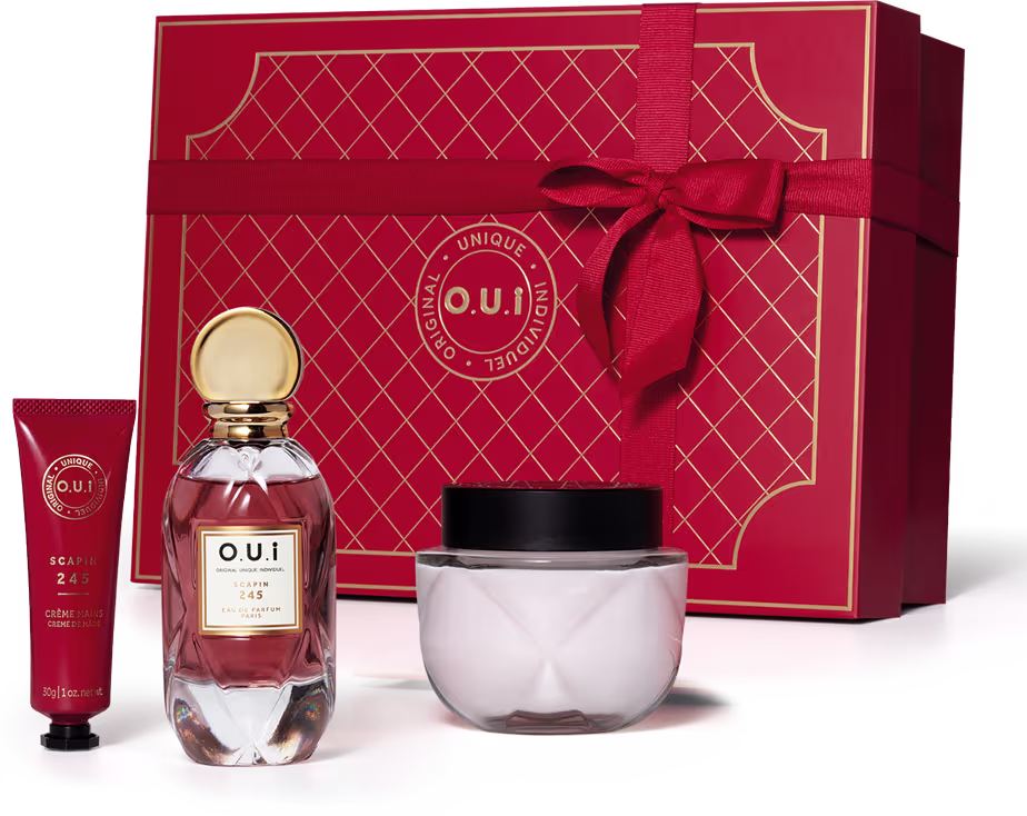 A imagem mostra um conjunto de produtos, com um frasco de eau de parfum, embalagem de creme hidratante corporal e creme para as mãos. O destaque é uma bela caixa de presente vermelha, com detalhes em relevo e um laço de fita vermelho.