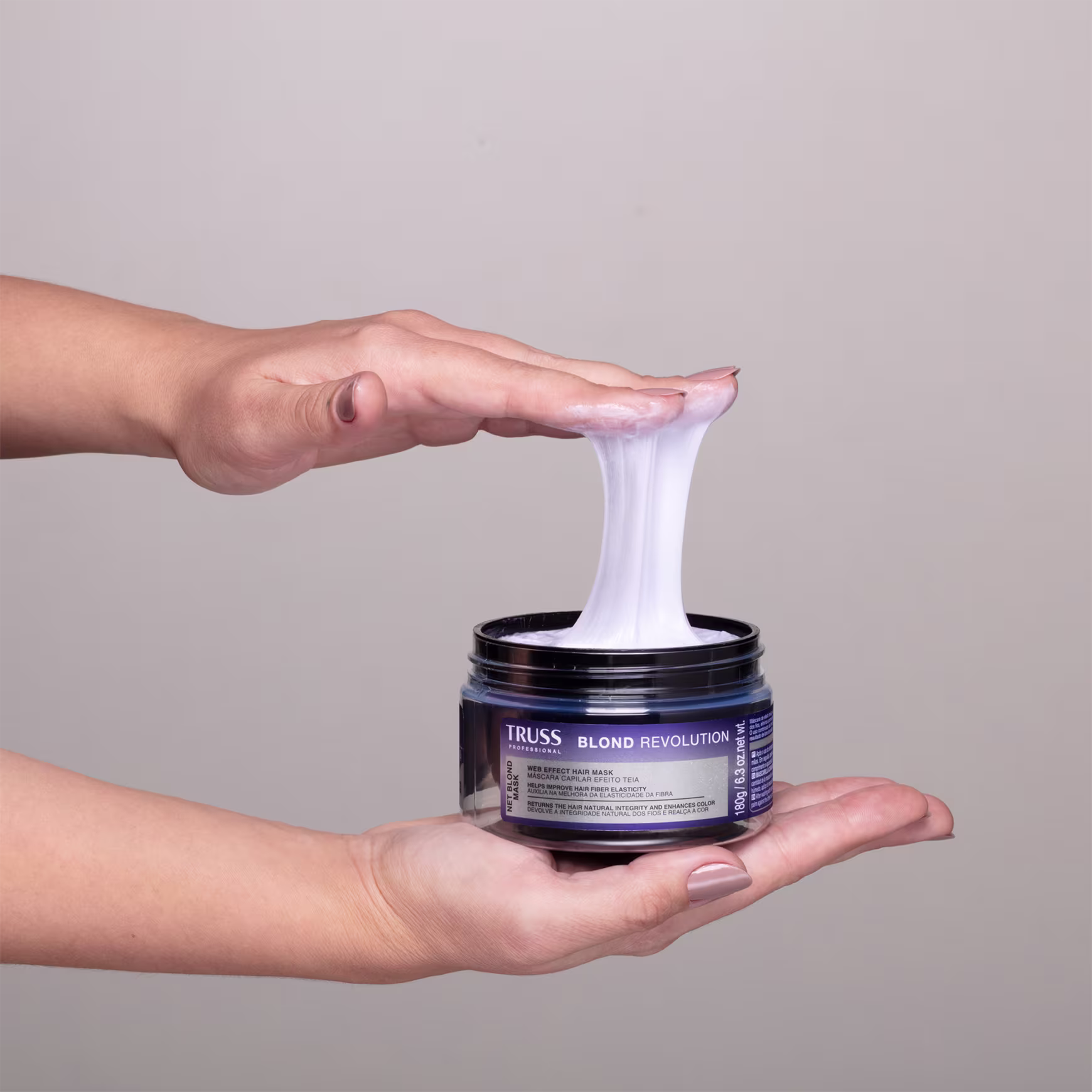 Imagem mostra uma mão segurando o pote da máscara e o outra mão pegando uma amostra do produto, exemplificando o efeito teia.
