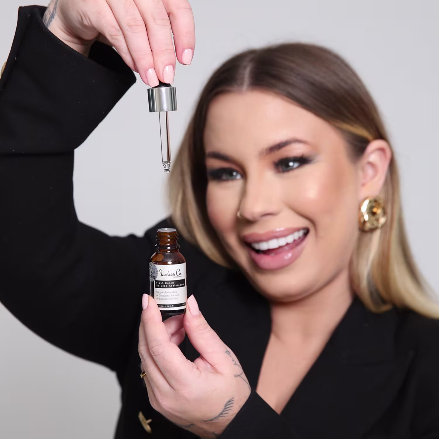 O produto de beleza mostrado na imagem é um frasco de vidro âmbar da marca Lashes Co. O frasco possui um conta-gotas na parte superior, indicando que se trata de um produto líquido.