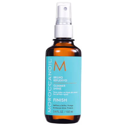 A imagem mostra o produto Moroccanoil Finish Glimmer Shine 100ml, frasco na cor âmbar com aplicador em spray. Traz rótulo azul com o logotipo "M" em laranja e texto "Brilho Reflexivo" e "Glimmer Shine" em branco.