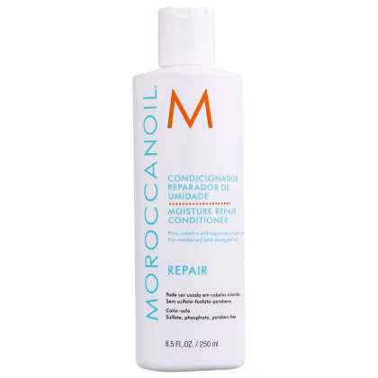 A imagem mostra o Condicionador Moroccanoil Moisture Repair 250ml, um frasco branco com letras em azul, laranja e preto e contém as informações do produto destacando que é livre de sulfatos, fosfatos e parabenos, seguro para cabelos coloridos.
