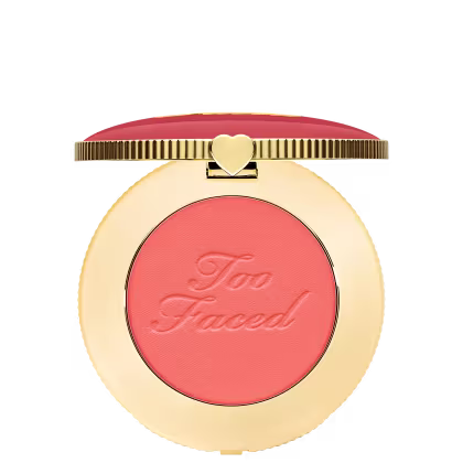 Blush compacto de maquiagem com embalagem redonda dourada. A tampa superior é rosa com a inscrição "Too Faced" em letras cursivas. Um pequeno coração dourado adorna o centro da tampa.