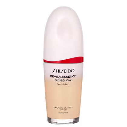 Base facial da marca Shiseido., Embalagem em forma de frasco plástico oval com uma faixa vermelha na parte superior. Rótulo indicando "Revitalessence Skin Glow Foundation" em letras pretas.