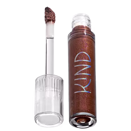 A imagem mostra a tampa da embalagem do gloss, com o aplicador virado pra cima, semelhante a uma tampa de batom, transparente e cilíndrica. Ao lado, o frasco do gloss, com o produto de cor marrom escuro e com a palavra KIND escrito na embalagem.