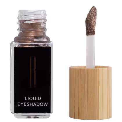 A imagem mostra um frasco aberto, retangular, transparente ao lado do aplicador de rosquear e com a ponta com a cor da sombra líquida, bronze. O rótulo do frasco é preto com logo da marca em dourado e "Liquid Eyeshadow" em branco no rodapé.