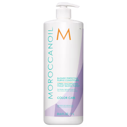 A imagem mostra o Condicionador Moroccanoil Color Care Blonde Perfecting Purple 1L, um frasco cilíndrico predominantemente branco, com detalhes em tons de roxo, laranja e azul. As informações do produto estão escritas em inglês e francês,