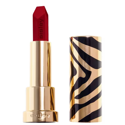 A imagem mostra um batom com embalagem dourada, aberto, com o batom à mostra e a marca do produto no rodapé. Ao lado, tem a tampa do produto, dourada com detalhes pretos.