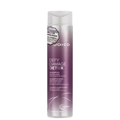 Shampoo detox Defy Damage da marca Joico. Embalagem cilíndrica roxa com detalhes prateados. Rótulo indicando que remove metais, minerais traço e cloro dos cabelos. Volume de 10.1 fl oz / 300ml.
