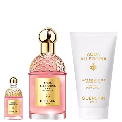 A imagem mostra um kit com perfume, versão travel size e body lotion. Os perfumes em frascos rosa com detalhes e tampas dourados, e o body lotion com embalagem branca.