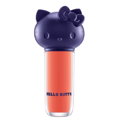Produto de maquiagem em formato cilíndrico com a cabeça da personagem Hello Kitty como tampa. A parte superior é azul escuro com detalhes que representam os olhos, orelhas e laço da Hello Kitty. É possível ver a cor do produto pelo corpo transparente.