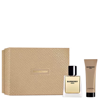 A imagem mostra um frasco de perfume retangular transparente com líquido âmbar, uma caixa de papelão bege estampada com o padrão monogramado da marca Burberry em relevo e um tubo de gel de banho da mesma linha.