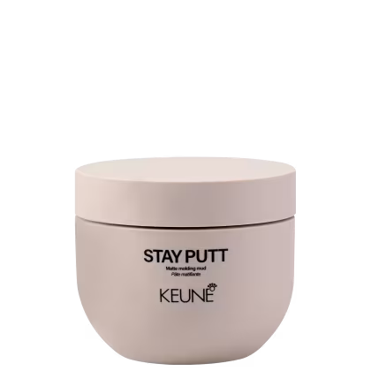 A imagem mostra a pasta finalizadora Stay Putt da marca Keune. Um pote arredondado bege claro fosco com tampa da mesma cor. Está impresso em letras pretas "STAY PUTT Matte molding mud Pâte matifiante".